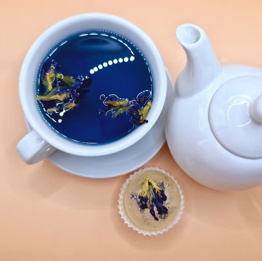 Cup of deep blue butterfly pea tea next to a white teapot