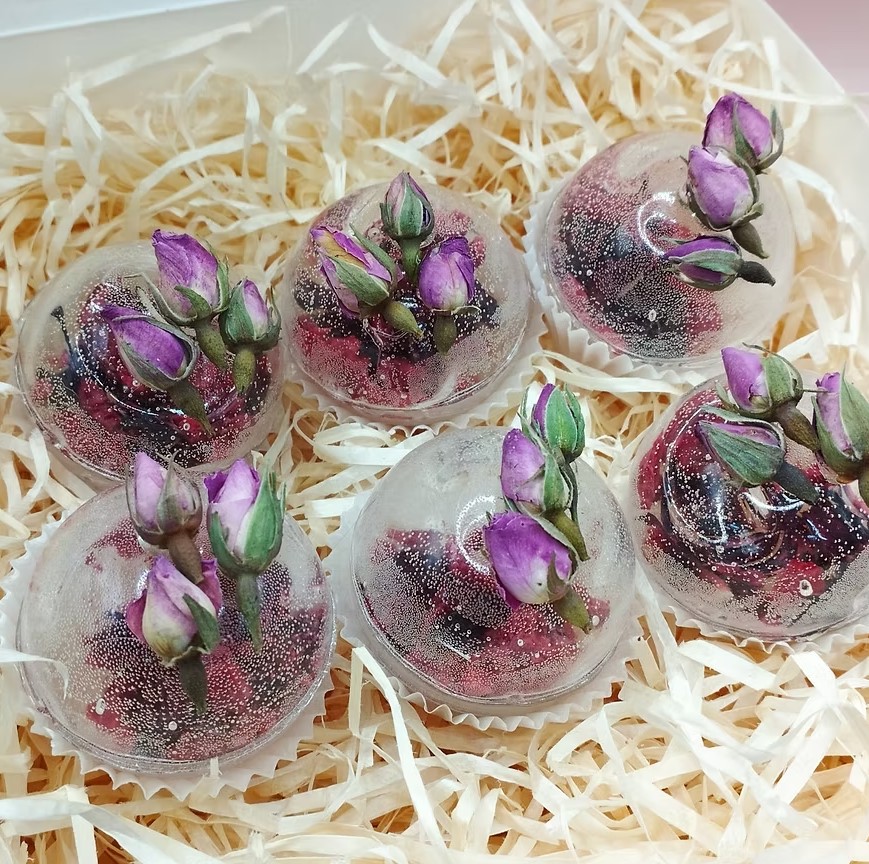 Six tea spheres with purple rosebuds in a box with wood-wool filling